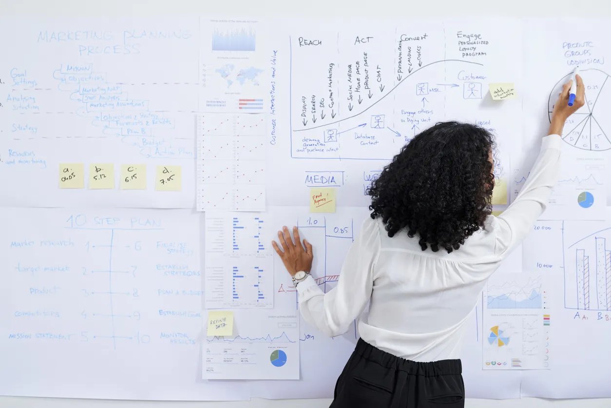 Une femme de dos qui écrit sur un tableau blanc