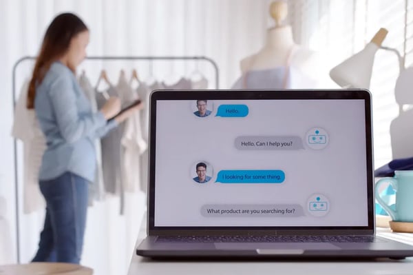 Conversation avec un chatbot sur l'interface d'un site internet e-commerce pour la vente de vêtements en ligne. En fond de la photo, nous voyons une femme avec un portant de vêtements.
