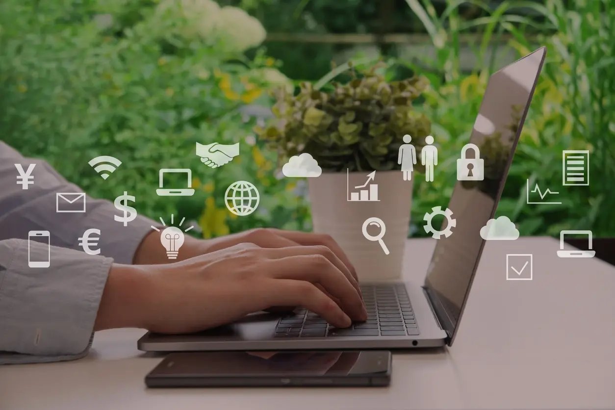 Une personne réalise un travaille sur son ordinateur. Cette personne est assise à son bureau devant une fenêtre donnant sur un jardin