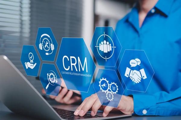 Sur la photo, nous voyons un homme qui utilise un ordinateur portable avec des icônes CRM représentant le support client, le service, l’établissement de relations, les ventes et les logiciels d’automatisation du marketing