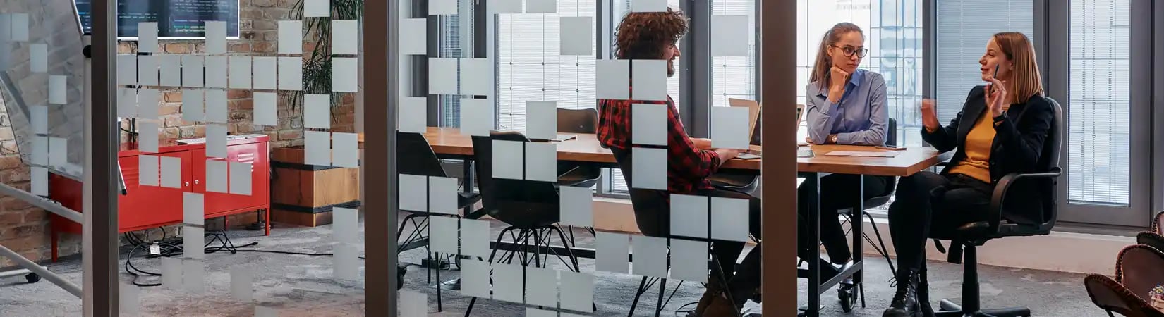 Un groupe de trois personnes travaillent à l'intérieur d’une salle de réunion